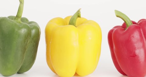Close up, Moving camera, Three colored bell peppers arranged in a row. Three bell pepper sites of the same size. On the white background.