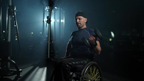 Disabled athlete in wheelchair performs exercises with dumbbells, man with disabilities performs the biceps exercise, handheld.