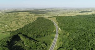 Aerial view of a landscape highway, Drone view of motorway in green fields light traffic, Vehicles on highway through scenic rolling green hills with trees and vegetation