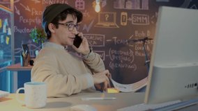 Friendly employee is speaking to client on mobile phone checking documents working late in creative office. Business conversation and modern technology concept. - Powered by Shutterstock - Get 15% off with code: PIKWIZARD15