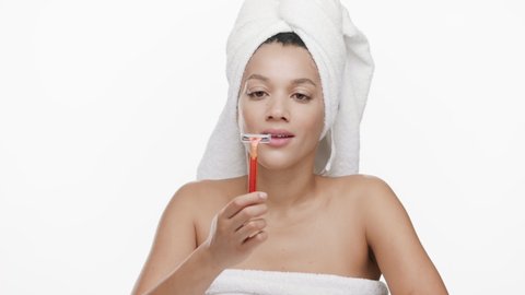 Funny good-looking young slim African American woman with a towel on her hair throws away orange razor on white background | Unwanted body hair removal concept