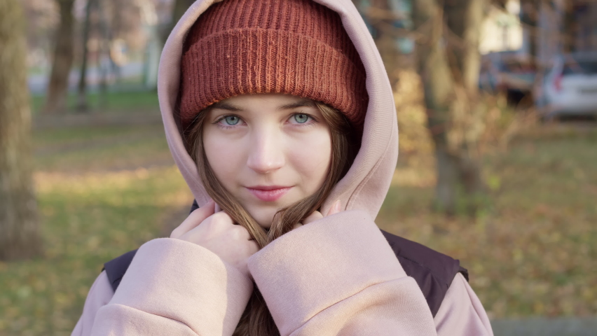 Portrait of a smiling and beautiful teenager girl in a hood standing in the street.