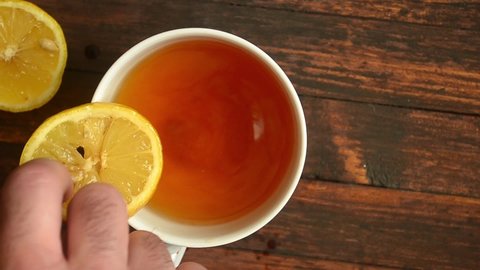 Man throws a slice of lemon into a cup of tea on wooden background