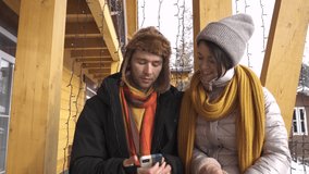 Two happy travel friends make video calls via smartphone in the mountains in winter trying to take selfies on their social networks or video stories with face masks.