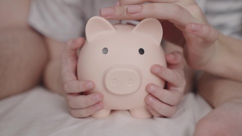 little child with mother and father throw coins of money at pig, happy family saving savings in piggy bank, childhood dream concept, little baby's home money, financial wealth savings, investing cash