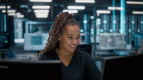 Portrait of African American Female IT Specialist Working on Desktop in Data Center. System Administrator Works on Web Services, Cloud Computing, Server Analytics, Cyber Security Maintenance, SAAS