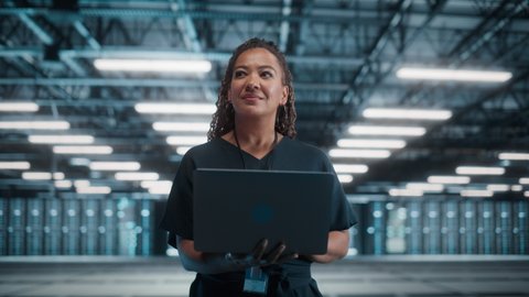 Concept Dolly Zoom Out: Portrait of Black Female Specialist Using Laptop in Big Data Center. Cinematic Shot with High-Tech Special Effect for Technology Science Breakethrough, Progress, Innovation