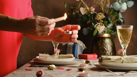 Valentines day table setting. Romantic table decoration. Saint Valentines day preparation, romantic date concept. Young woman lights candles on served table. 