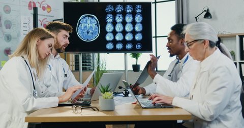 Good-looking confident experienced purposeful diverse team of neurologists working together in modern medical room with medical reports,medicine concept