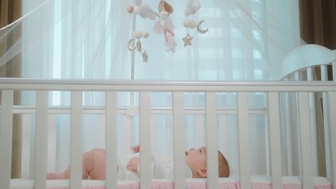 Attractive and cute baby girl while laying down on her baby cot and looking concentrated up at the cot toys. Shot on ARRI Alexa Mini.