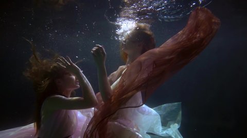 passionate elegant lesbian couple in dresses hugging underwater, romance in the depths of the pool, slow motion