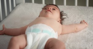 Newborn baby in a diaper lies on its back in a light child crib. Neonate toddler in a nursery room. Concept of Childhood, New Life, Parenthood. High quality 4k video. Shot with RED camera.