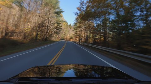 Driving a car on Vermont asphalt road in Autumn season. Colorful trees by the road. POV with sunlight