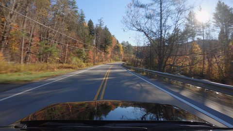 Driving a car on asphalt road in Vermont, United States .Autumn season, colorful trees by the road. POV with sunlight