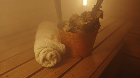 Bucket with bath broom and towel in sauna.