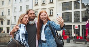 Caucasian youngsters taking photo and video on smartphone on street in city. Good-looking girsl and guy wriggling to camera and laughing outdoors. Technology, youth, entertainment concept.