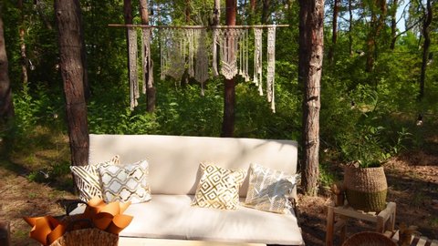 Lounge photo zone with diy sofa and table of cargo pallets in boho style on outdoor wedding ceremony venue in pine forest. Bohemian decor.