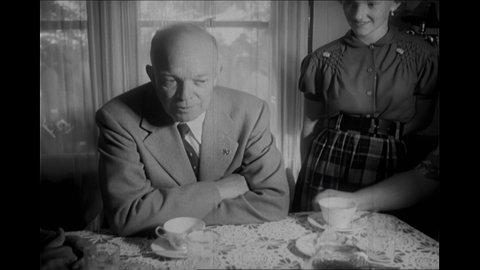 1950s: Titles. Dwight Eisenhower riding farm equipment through crowd. Crowd of press. Eisenhower shakes hands with woman. Girls wearing helmets. Eisenhower with family at table. Eisenhower talking.