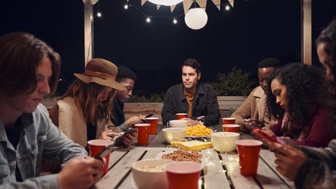 Caucasian male sitting feeling lonely while his multi-ethnic group of friends text at a rooftop party