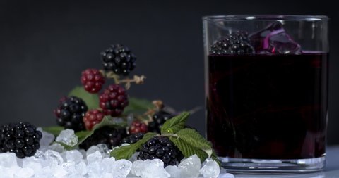 Blackberry juice is poured into a crystal transparent glass on ice with red, natural blackberries on a black background, vitamin and delicious sweet juice. Fimled on cinema camera, 8K downscale. 4K.