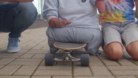 Woman with congenital malformations of the upper and lower endpoints on a skateboard surrounded by friends using the phone. CZ, Kladno, Armenska, 4.8.2021.