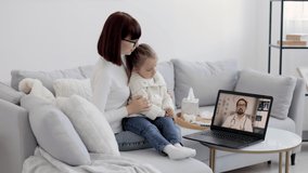 Doctor therapist consulting young woman about disease of her daughter during online appointment on laptop at home. Mom and daughter on conference video call with Male doctor working from his office