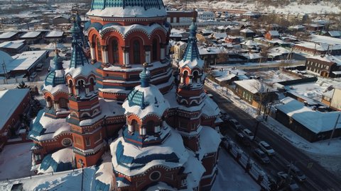 Flight close to amazing decorated dome facade of Kazan Cathedral Irkutsk winter Russia orthodox tample in downtown. Old authentic wooden houses historical street, road traffic. Travel landmark