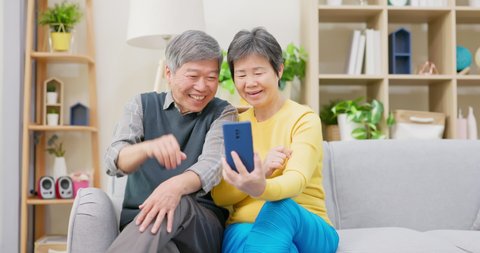 asian elderly couple have video call by mobile phone in living room at home