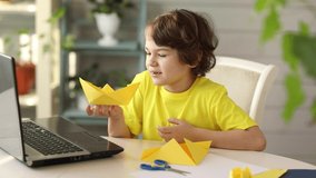 a boy in a yellow T-shirt at an online origami workshop, a paper boat