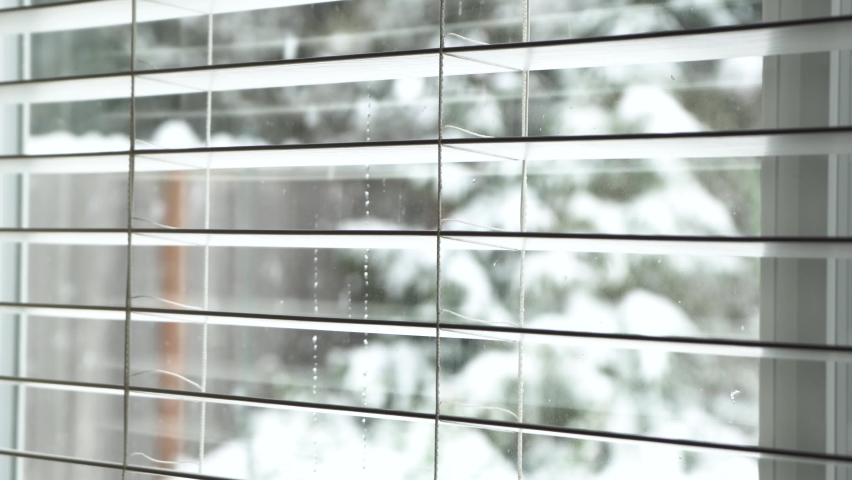 Rack focus of snow falling in backyard, looking out through window blinds. | Shutterstock HD Video #1084244575