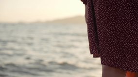 Woman standing alone on sunny sandy sunset tropical beach outdoors. Close-up view 4k slow motion video footage of skirt of woman blown by wind