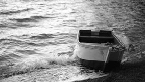 Black and white stock 4k video footage of old empty wooden fishing boat floating on waves of sea on seashore in evening