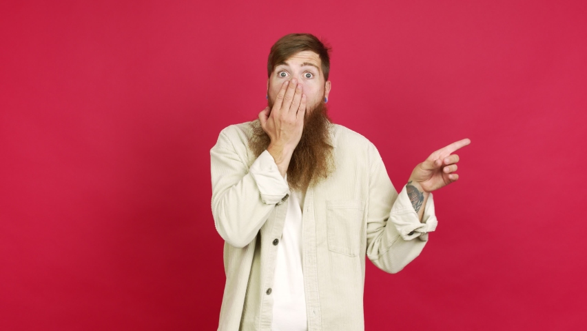 Redhead man with long beard pointing to the side and presenting a product while smiling over isolated background
