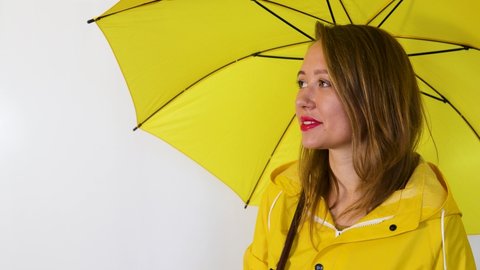 A girl in a yellow raincoat under an umbrella stretches out her hand to the rain. Isolated on white background.