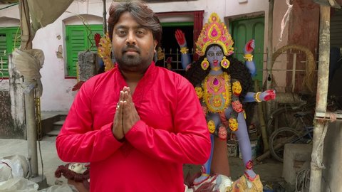 Kolkata , West bengal , India - 11 27 2021: Indian man in red kurta worshiping lord kali looking at the camera 