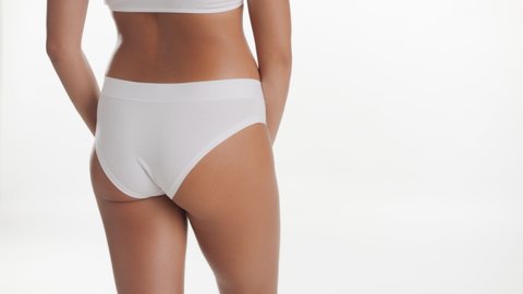 Horizontal medium shot of African American slim good-looking woman in white underwear strokes her hip putting her hand on her waist on white background | Anti cellulite concept