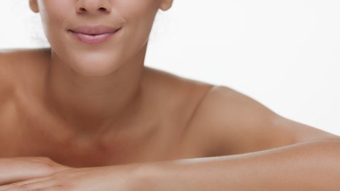 Good-looking slim young brunette African American woman with nude shoulders put her head on her arm smiling for the camera on white background | Flawless skin concept