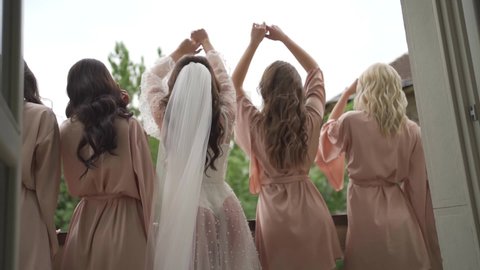 Bride and her bridesmaids are having fun on balcony. Morning meeting of the bride on the wedding party. Beautiful dresses. Slow motion.