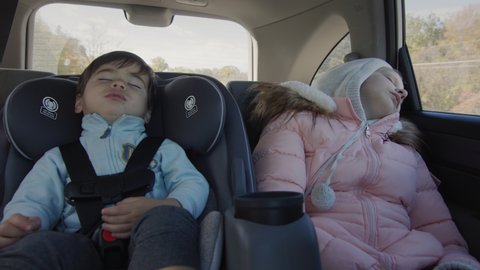 Sleeping children drive in the back seat of the car. Asian baby sleeps in a child car seat, a girl naps next to her.