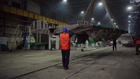 Transportation of a Large Metal Component By a Crane. Three Operators Guiding and Supervising the Process. Railcar Wagon Manufacturing. Inside a Modern Facility. Railroad Equipment.