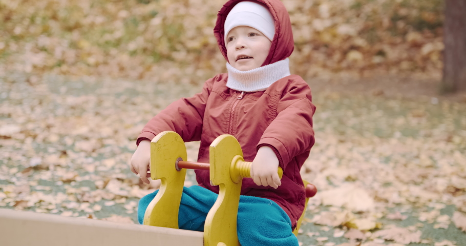 Small, cute child rides on a swing in the yard on a walk with his parents. The carousel rolls the baby, the baby is happy and smiling. Lifestyle and active recreation