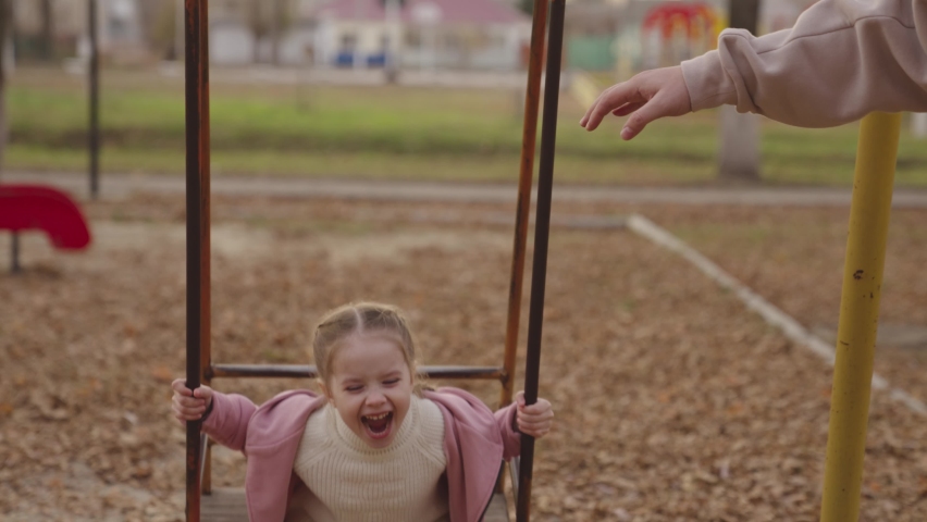 mother pushes the swing up and cheerful child laughs, happy family, kid play on the swing in autumn playground, children's entertainment outside, life of little people on weekends, chidhood dream fly Royalty-Free Stock Footage #1084268011