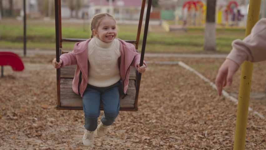 mother pushes the swing up and cheerful child laughs, happy family, kid play on the swing in autumn playground, children's entertainment outside, life of little people on weekends, chidhood dream fly Royalty-Free Stock Footage #1084268011