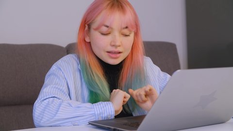 Freelancer girl with dyed hair stretching arms and typing text on laptop keyboard. Young woman with colored hair doing distant free lance work during lockdown