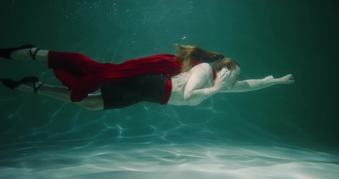 Amazing cinematic slow motion, young business woman with red superhero cape swims underwater on phone call slow motion.