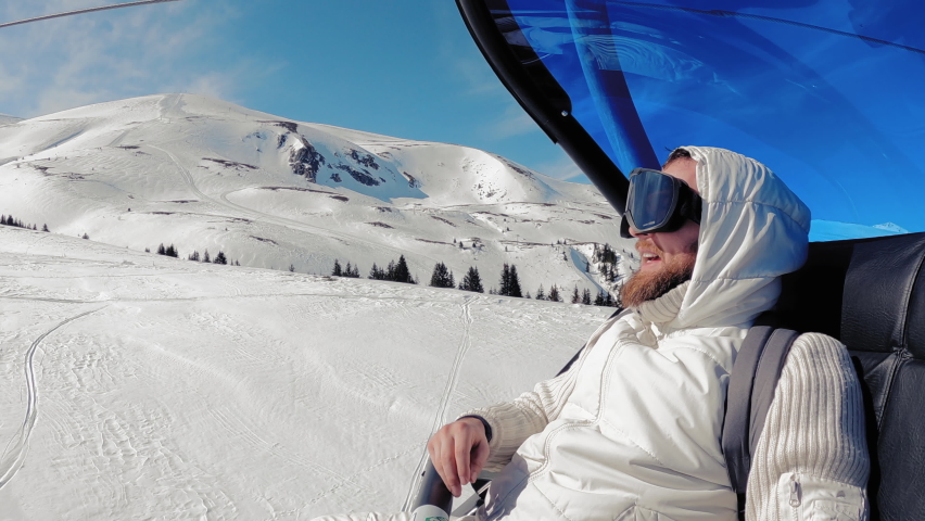 Smiling hippie man with a beard with skis riding on a ski lift, slow motion