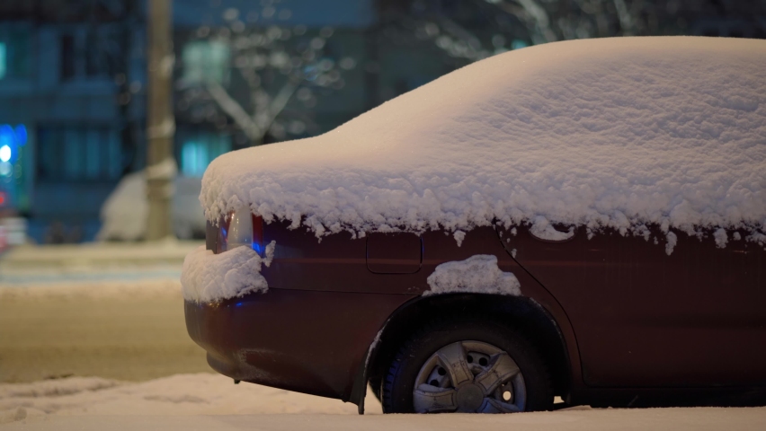 Snow covered vehicle, side view. night city street after snowfall. snowу car parked by the road side. red car in snow stands at the winter road edge. after blizzard winter evening scene