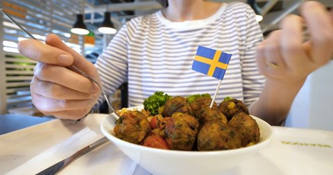 Lyon, France - Circa 2019: Front view of woman eating delicious meatballs at the Ikea Food restaurant with the Swedish tiny flag on top of them