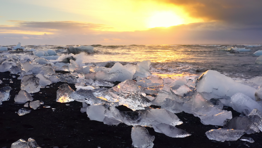Icebergs shining on a black beach during golden hour. Sunrise on Diamond Beach in Iceland. Clear ice crashed by Ocean waves. Climate Change Global Warming problem. Royalty-Free Stock Footage #1084282924