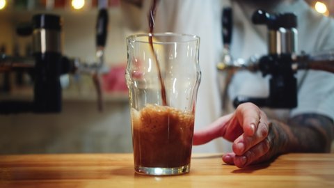 Barman pouring nitrogen beer into glass close-up. Bartender pours alcohol foamy drink in mug. Fresh beverage on bar counter background in pub.